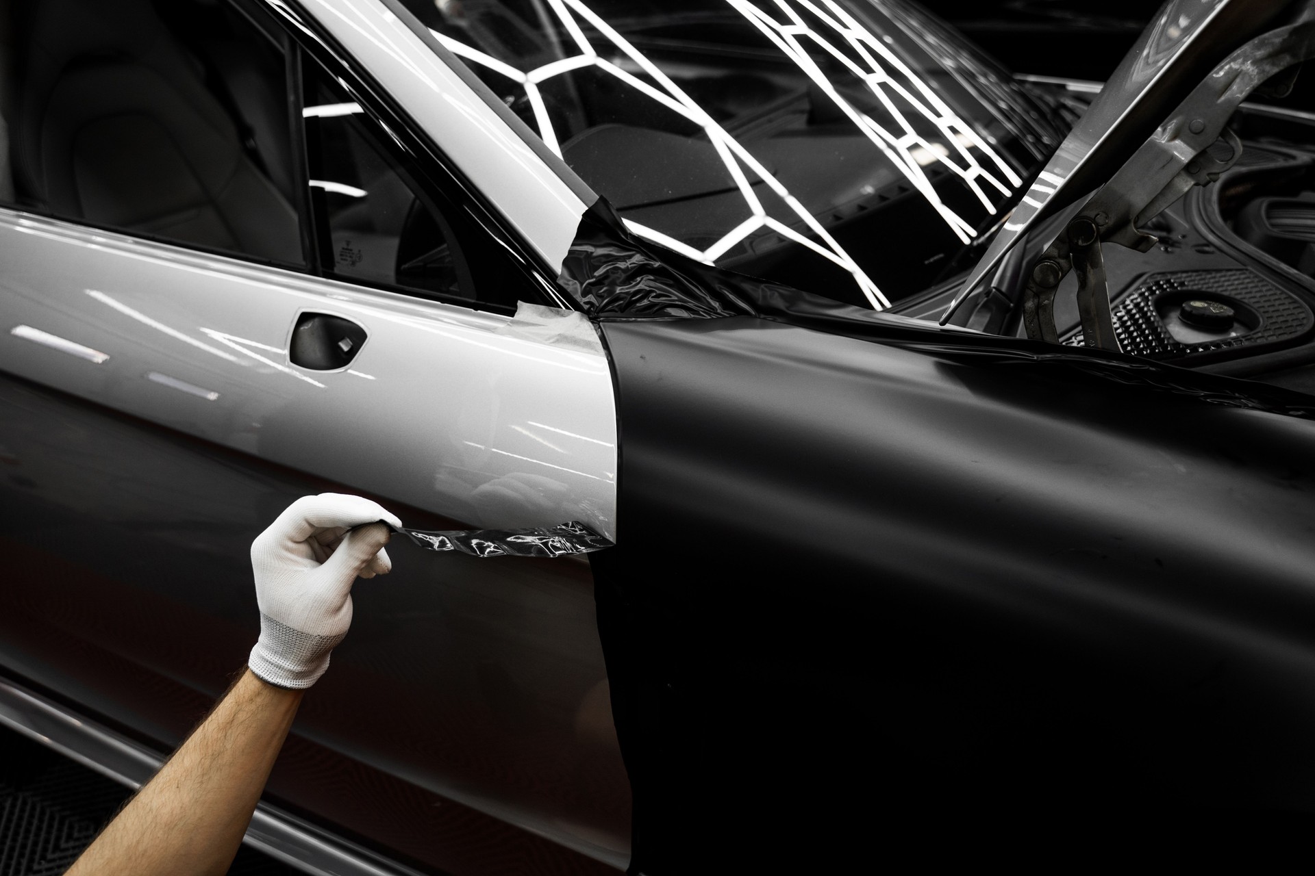 Car wrap application changes vehicle appearance. Full Panel Car Vinyl Wrapping. Large-scale vinyl wrap installation transforms the vehicle exterior with matte black film.